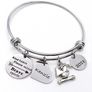 Silver Stainless Steel Engraved charm bracelet. circle disc engraved with "Kind Heart. Fierce Mind. Brave Spirit" with a arrow image. Next is a heart name charm. next is a graduation cap and tassel charm. lastly is a circle charm with the year "2021" engraved. All charms are attached to a triple loop stainless steel bangle bracelet