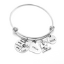 Silver Stainless Steel Engraved charm bracelet. circle disc engraved with "Not all who wander are lost" with a dandelion image. Next is a heart name charm. next is a graduation cap and tassel charm. lastly is a circle charm with the year "2021" engraved. All charms are attached to a triple loop stainless steel bangle bracelet