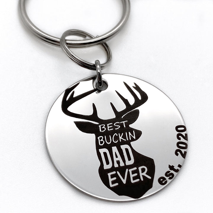 1.25 inch shiny stainless steel disc engraved with a buck deer head shiloutte and teh verbaige "best bucking dad ever" engraved with "est 2020"