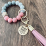 Pink, White, Grey round silicone beaded Wristlet with matching leather lobster clasp keychain hook. Attached is a rose gold charm tag engraved with "Blended and Blessed" with an arrow heart image and personalized with the names "Emmett, Emily, and Evan"