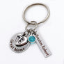 silver stainless steel keychain. circle disc engraved with great meme. baby's feet charm lays on top. besides is a december stone. a 1 inch rectangle tage engraved with the name Braxton Robert.