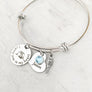 silver bangle charm bracelet with a 3/4" round engraved disc with the image of a baby sleeping under angel wings and the verbiage "I carry you in my heart" next to it is a 3/4" heart engraved with the name "Jason" and. a blue march birthstone. Last is an angel wing charm.