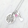 Round pendant necklace engraved with the phrase "like roots to a tree you are connected to my heart". a tree of life charm lays on top of the engraved round pendant. Next to the pendant is a rectangle charm engraved with "unbiological sisters". attached to the main pendant is a october birthstone. all charms are attached to a stainless steel silver cable chain.