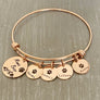 Rose Gold Bangle adjustable charm bracelet with a 3/4" engraved disc with a bear paw print, mountain range scene and verbiage "Mama Bear" along with three 1/2" name tags engraved with a cub paw print and the names Naima, Brandon Jr, Leilana, Keanu