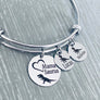 silver stainless steel triple loop bangle bracelet. first round charm measures .75 inches and is engraved with a trex dinosaur image and on open heart frame with "Mama Suarus". Next charm measures 1/2 inch and is engraved with a baby trex and the name lucas. next charm is engraved with a baby trex and the name nicholas
