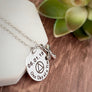 Round silver 7/8" pendant charm necklace engraved with "One Day at a Time", the AA sobriety symbol and the recovery date of 06.01.19. Next to the round charm is a silver religious cross charm. Both pieces are attached to a stainless steel cable chain