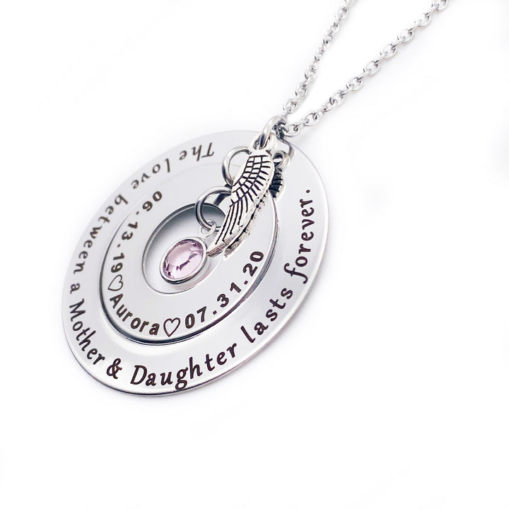 Silver Round 2 disc necklace. outside washer is engraved with "the love between a mother and daughter lasts forever." The inner washer is engraved with the birthdate 06.13.19 a heart image the name Aurora, heart image, and death date 7.31.20. June birthstone dangles inside the washer and angel wing charm on top. All charms and pendants hang from a stainless steel cable chain