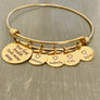 stainless steel yellow gold bangle charm bracelet with a 3/4 inch disc engraved with "your first breath took mine away". 1/2 inch name discs with open heart image above the engraved name.