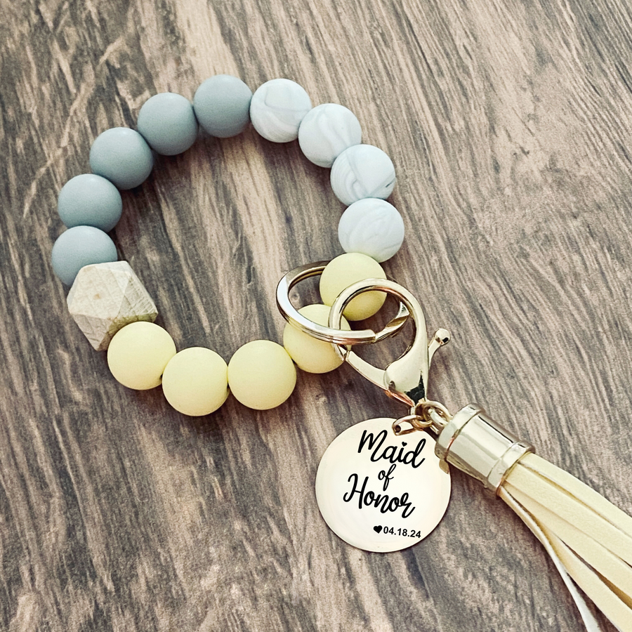 Yellow, Marble and grey silicone beaded wristlet with matching lobster clasp leather tassel. Attached a large stainless steel circle charm tag engraved with Maid of Honor, a small heart silhouette  and the wedding date 4.18.24