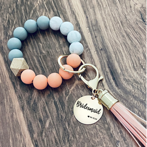 Coral, Marble and grey silicone beaded wristlet with matching lobster clasp leather tassel. Attached a large stainless steel circle charm tag engraved with Bridesmaid a small heart silhouette  and the wedding date 4.18.24