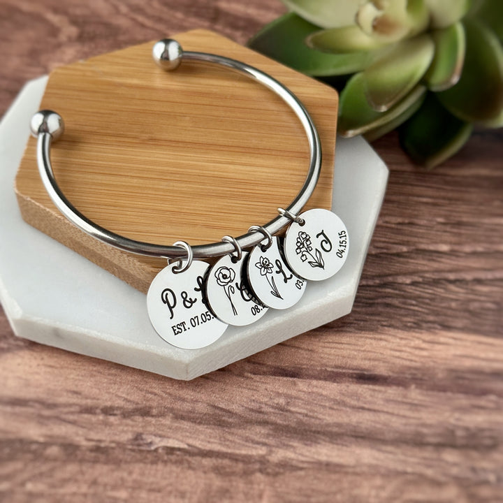 silver charm bracelet with 4 charms. main charm is engraved with parents first name initial and wedding date. next three charms are engraved with child's birth month flower initial, and date of birth
