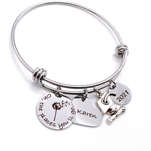 Silver Stainless Steel Engraved charm bracelet. circle disc engraved with "Oh, the places you'll go..." with a dandelion image. Next is a heart name charm. next is a graduation cap and tassle charm. lastly is a circle charm with the year "2021" engraved. All charms are attached to a triple loop stainless steel bangle bracelet