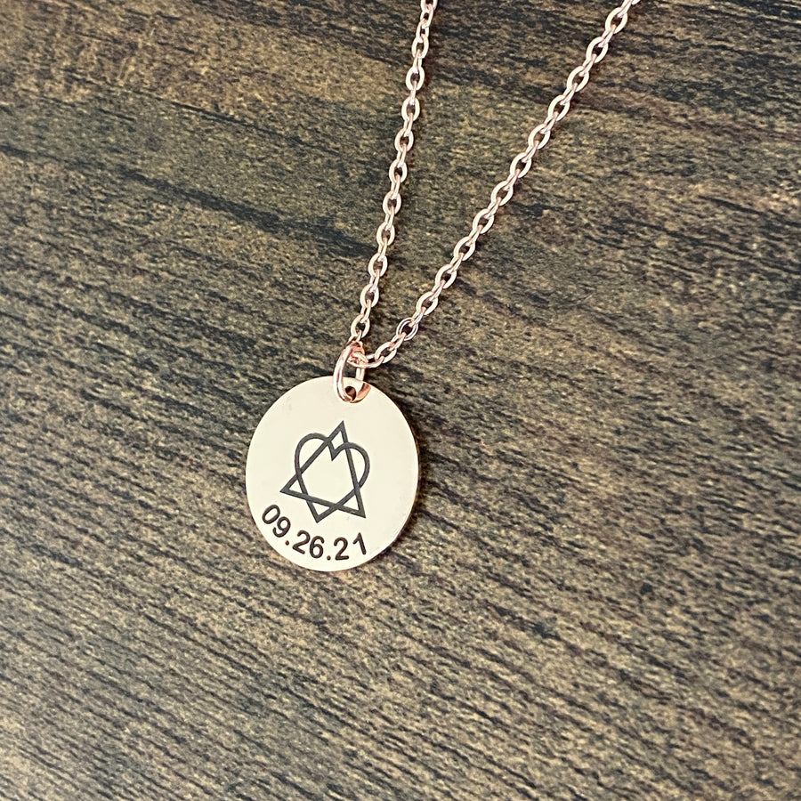 Round 3/4 inch engraved rose gold pendant necklace with the adoption traid symbol and the gotcha date 09.26.21 hanging from a cable chain with lobster clasp.