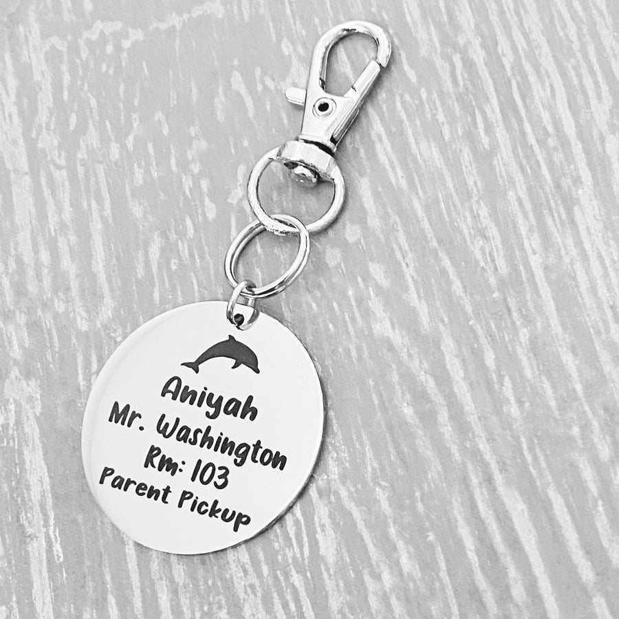 silver engraved stainless steel backpack tag keychain. engraved with a Dolphin Image, Name Aniyah. Teachers name Mr. Washington Room number 103. and Parent Pickup