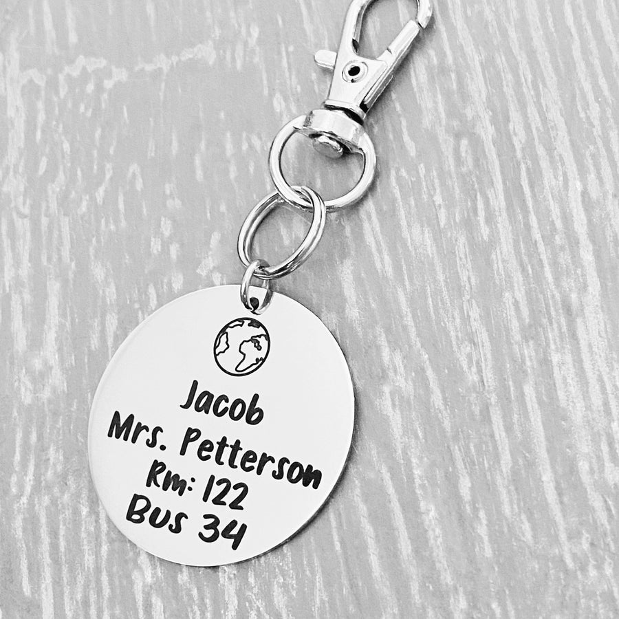 silver engraved stainless steel backpack tag keychain. engraved with a Rocket Image, Name Jacob. Teachers name Mrs Petterson. Room number 122. and Bus 34