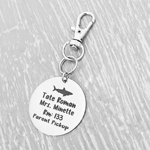 silver engraved stainless steel backpack tag keychain. engraved with a Shark Image, Name Tate Roman. Teachers name Mrs Minette. Room number 133. and Parent Pickup