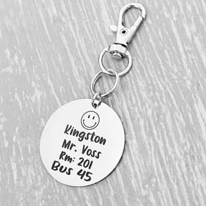 silver engraved stainless steel backpack tag keychain. engraved with a Smiley Face Image, Name Kingston Teachers name Mr Voss. Room number 201. and Bus 45