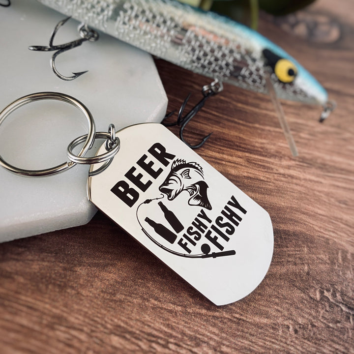 Silver dog tag keychain engraved with "Beer Fishy Fishy" and a bass fish biting a fishing pole hook