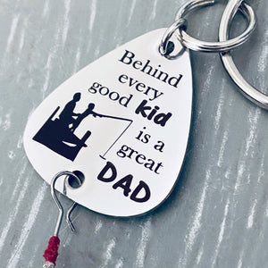 Silver stainless steel fishing lure keychain engraved with the phrase, "Behind every good kid is a great dad" along with an image of a father helping his son fish off a dock.