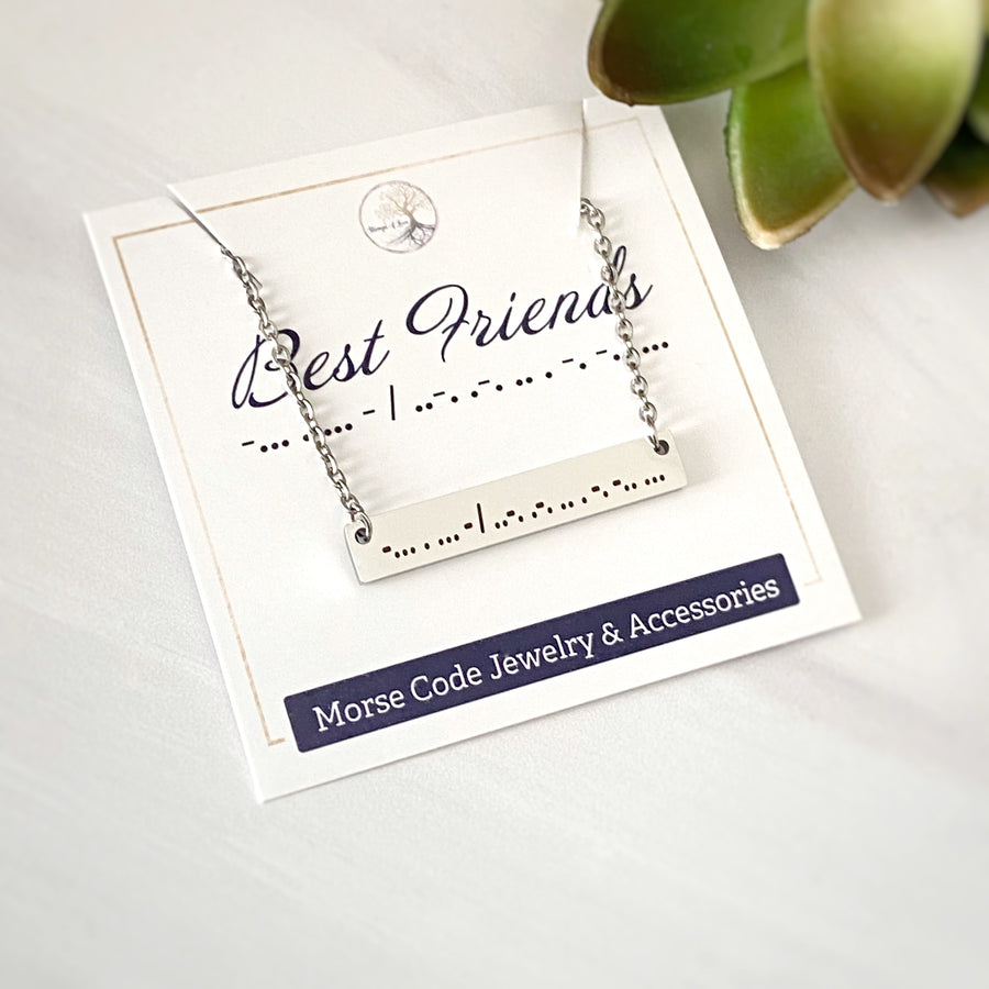 silver stainless steel horizontal bar necklace engraved with "Best Friends" in Morse Code and attached to a cable chain with lobster clasp. The necklace is on a packaging card that indicates the morse code means best friend.
