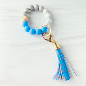 Medium Blue, marble, grey silicone beaded bracelet. A rose gold lobster key hook with medium blue tassel is attached to the wristlet