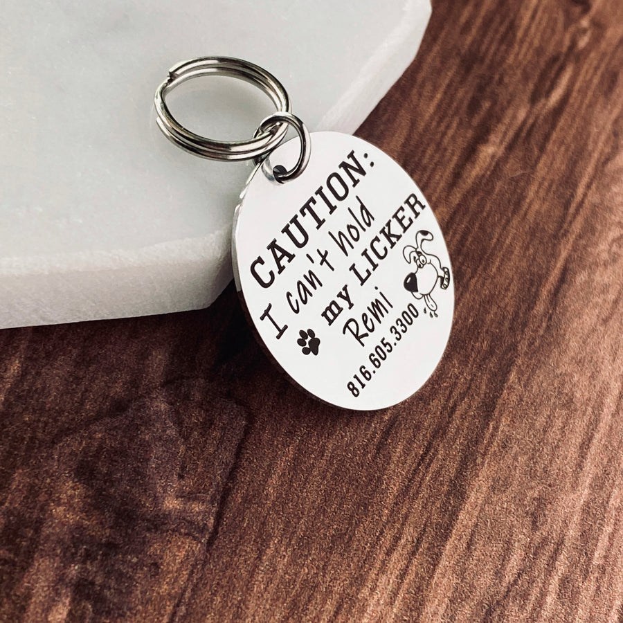 Silver stainless steel dog collar id tag with black engraving "caution I can't hold my licker" with a picture of a licking dog, pets name and telephone number