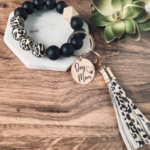 Cheetah and black round silicone beaded wristlet bracelet with a large lobster clasp keychain with matching leather tassel and charm tag engraved with Dog Mom and open heart dog paw print.