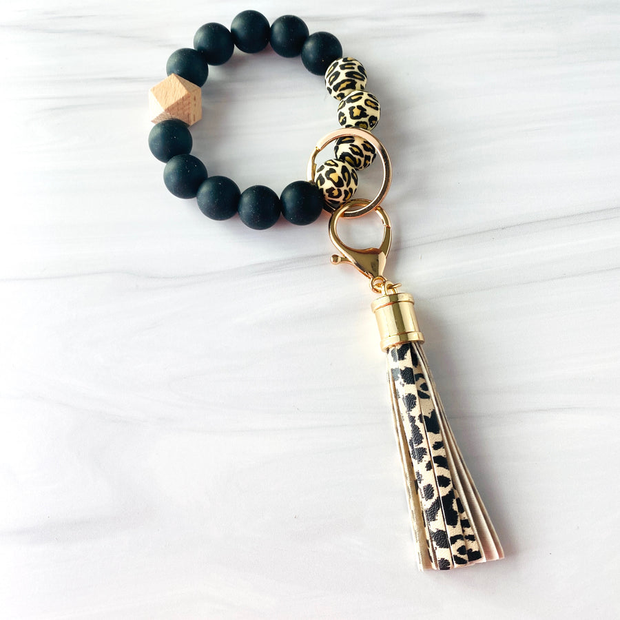 Cheetah print, and black  silicone beaded bracelet. A rose gold lobster key hook with cheetah print tassel is attached to the wristlet