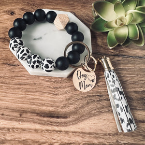 Black and cow print round silicone beaded wristlet bracelet with a large lobster clasp keychain with matching leather tassel and charm tag engraved with Dog Mom and open heart dog paw print.