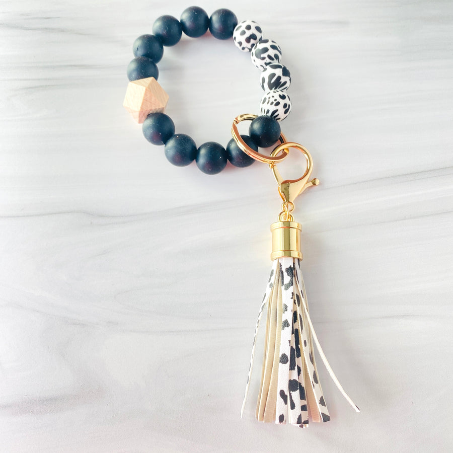 Cow print and black silicone beaded bracelet. A rose gold lobster key hook with cow print tassel is attached to the wristlet