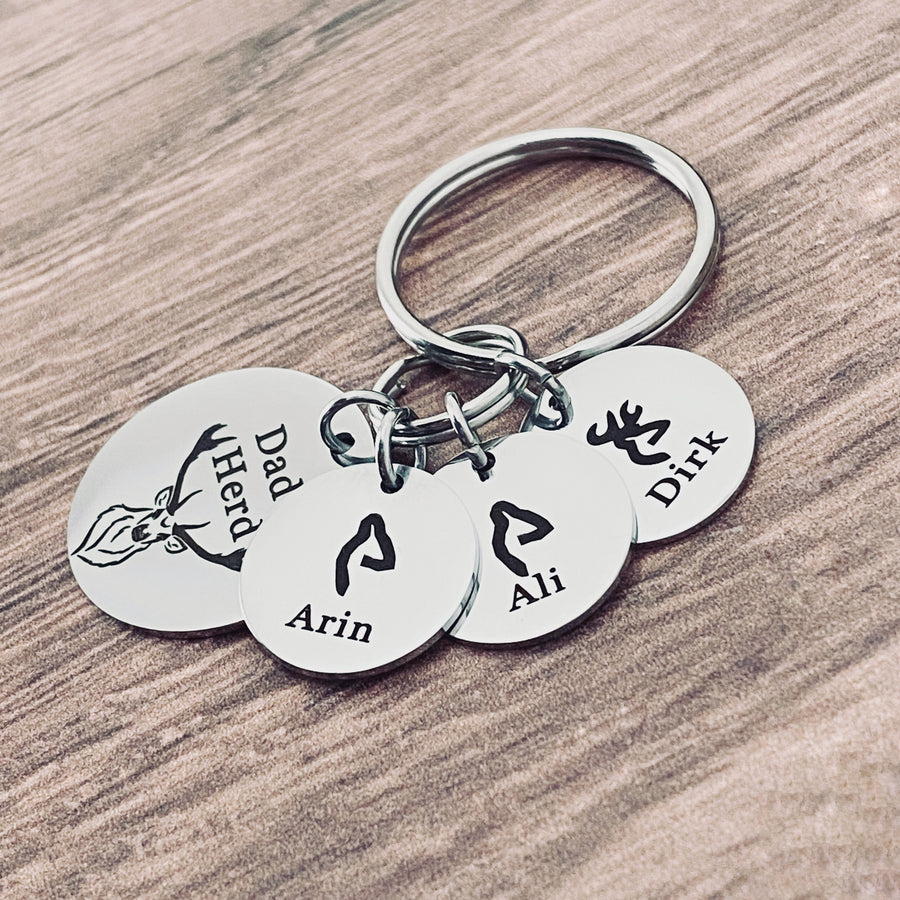 silver stainless steel 7/8" round keychain engraved with a Buck Deer image and "Dad's Herd". Next to the main charm are 3 small 1/2" name tags. first tag has a fawn deer head image and name Arin. Second charm with a girl deer charm with name Ali. third charm is a boy deer and the name Dirk.