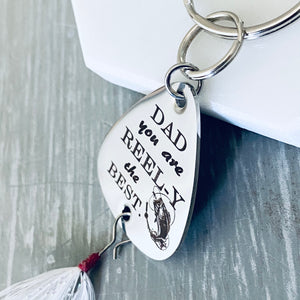 Side view of a 1 inch silver stainless steel fishing lure keychain. Engraved with DAD you are REEL-Y the BEST" attached to a durable steel keyring and fishing feather.