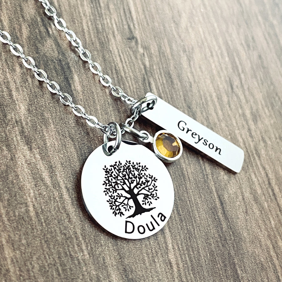 Silver 3/4" round pendant that is engraved with a tree of life symbol and the name "doula". next is a november birthstone. also a rectangle charm engraved with name "Greyson". all charms are connected to a silver cable chain