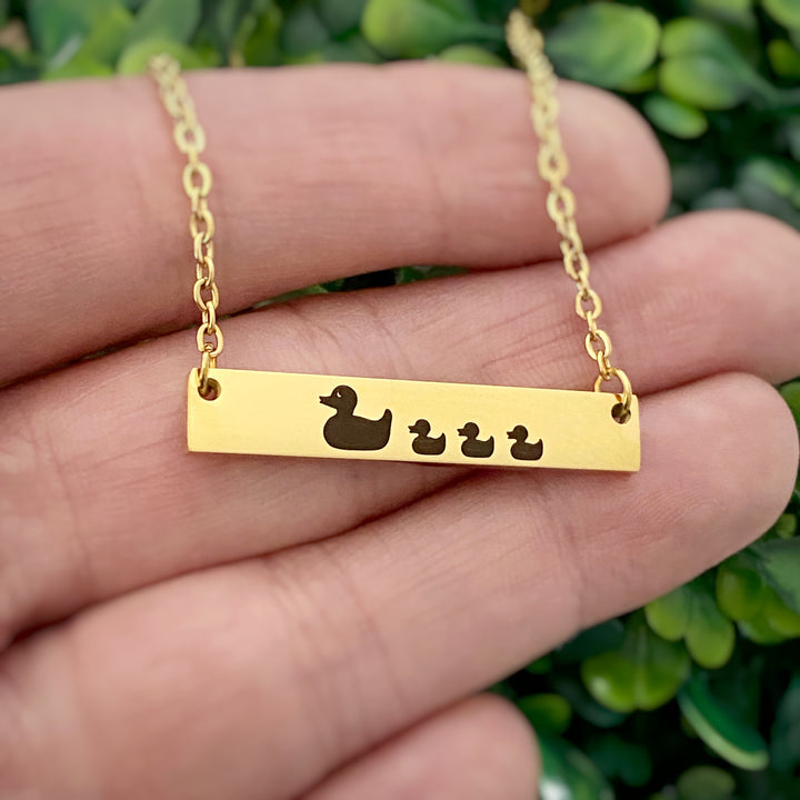 yellow gold duck bar necklace engraved with one mom duck and 3 baby ducklings attached to a yellow gold cable chain with lobster clasp