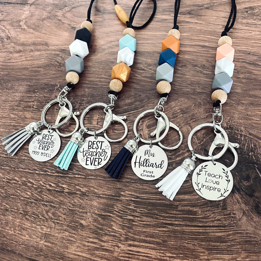 4 different color pattern lanyards in boho, coral, black, and mint color patterns attached to a lobster clasp key hook and matching tassel. 4 different charm tags.Best teacher ever with teacher's name, best teacher ever generic, teachers name and fourth grade, and teach love inspire.