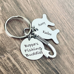 Silver engraved personalized fishing keychain. Main tag is engraved with "Boppa's fishing buddy". Next is a silver fishing hook. Next is a silver engraved fish tag charm with the name "Kailee" and another fish charm engraved with the name "Avery""