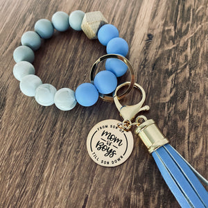 medium blue round silicone beaded wristlet with large leather tassel and charm tag engraved with "mom of boys. from son up to son down"
