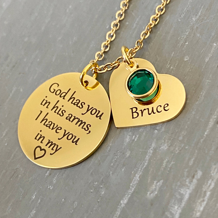 Yellow Gold Necklace with 3/4 inch round pendant engraved with "God has you in his arms, I have you in my heart". Next to the disc is a 3/4 inch heart engraved with Bruce and a green may stone. Pendants are attached to a cable chain