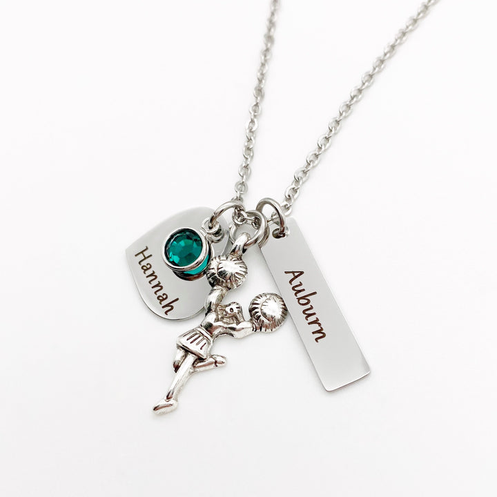 Silver stainless steel 3/4" heart charm engraved with cheerleaders name "Hannah", May Birthstone, Cheerleader Charm, and a rectangle cheer team name tag. All charms are attached to a silver stainless steel cable chain with lobster clasp.
