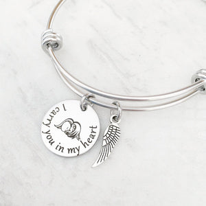 silver bangle charm bracelet with a 3/4" round engraved disc with the image of a baby sleeping under angel wings and the verbiage "I carry you in my heart"  next is an angel wing charm.