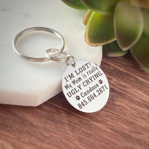 Silver stainless steel round dog collar id tag engraved with "I'm Lost! My mom is really ugky crying" with the pet's name candice and a phone number.
