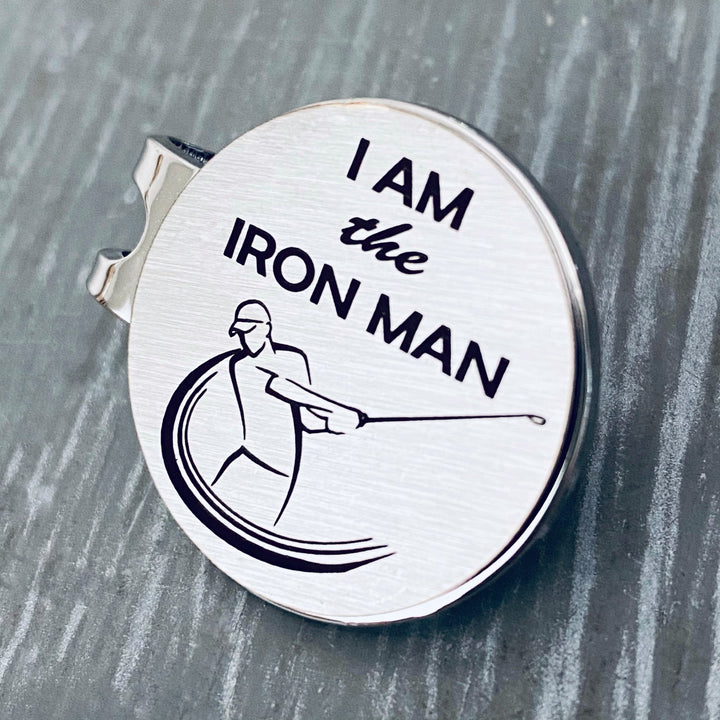 1 inch brushed silver stainless steel golf ball marker on magnetic hat clip. Marker is engraved with the image of a golfer swinging a club and the phrase "I AM the IRON MAN
