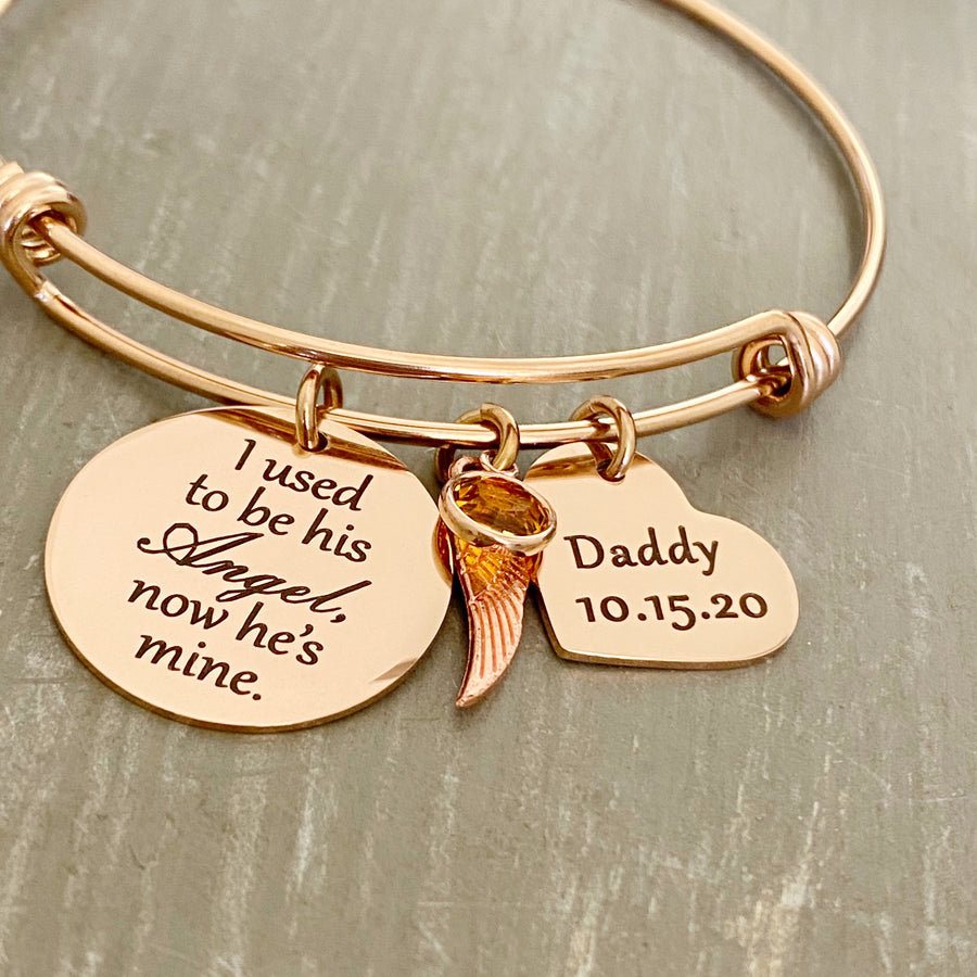 rose gold bangle charm bracelet with an engraved 7/8" disc "I used to be his Angel, now he's mine", an angel wing charm, november birthstone, and a 3/4" heart engraved with "daddy and 10.15.20""