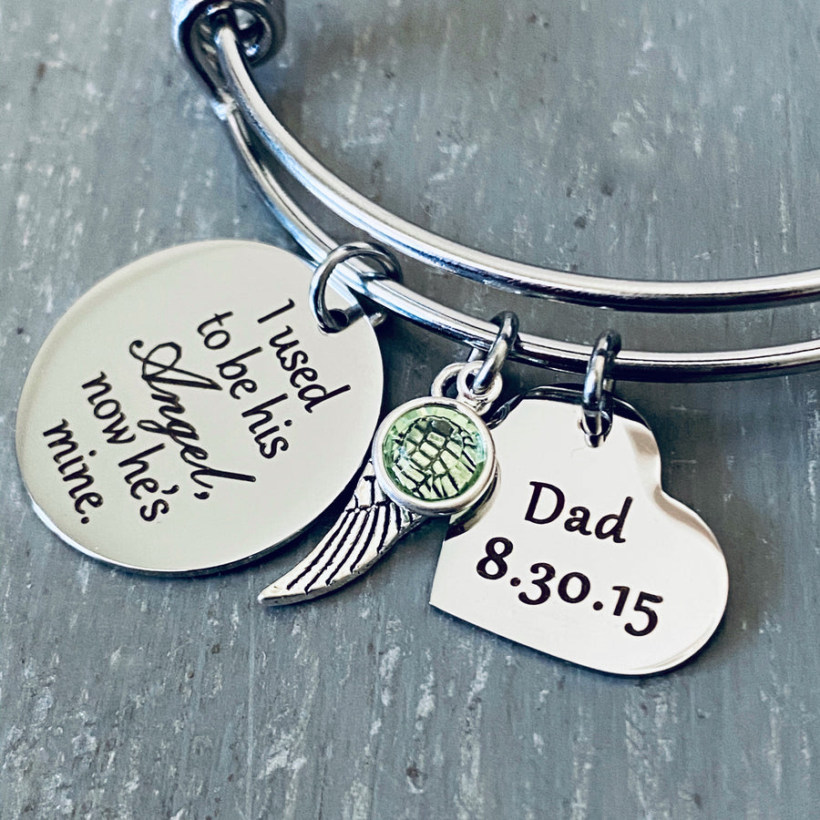 Silver bangle charm bracelet with an engraved 7/8" disc "I used to be his Angel, now he's mine", an angel wing charm, august birthstone, and a 3/4" heart engraved with "dad and 8.30.15"