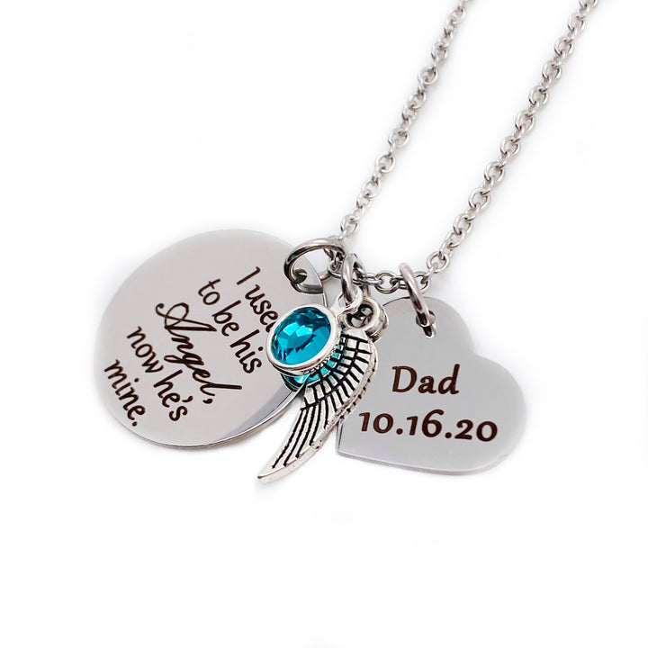 silver stainless steel 7/8" round disc engraved with "I used to be his Angel, now he's mine", an angel wing charm, a december blue birthstone, a 3/4" engraved heart with "Dad and death date "10.16.20". all charms are attached to a silver stainless steel cable chain.