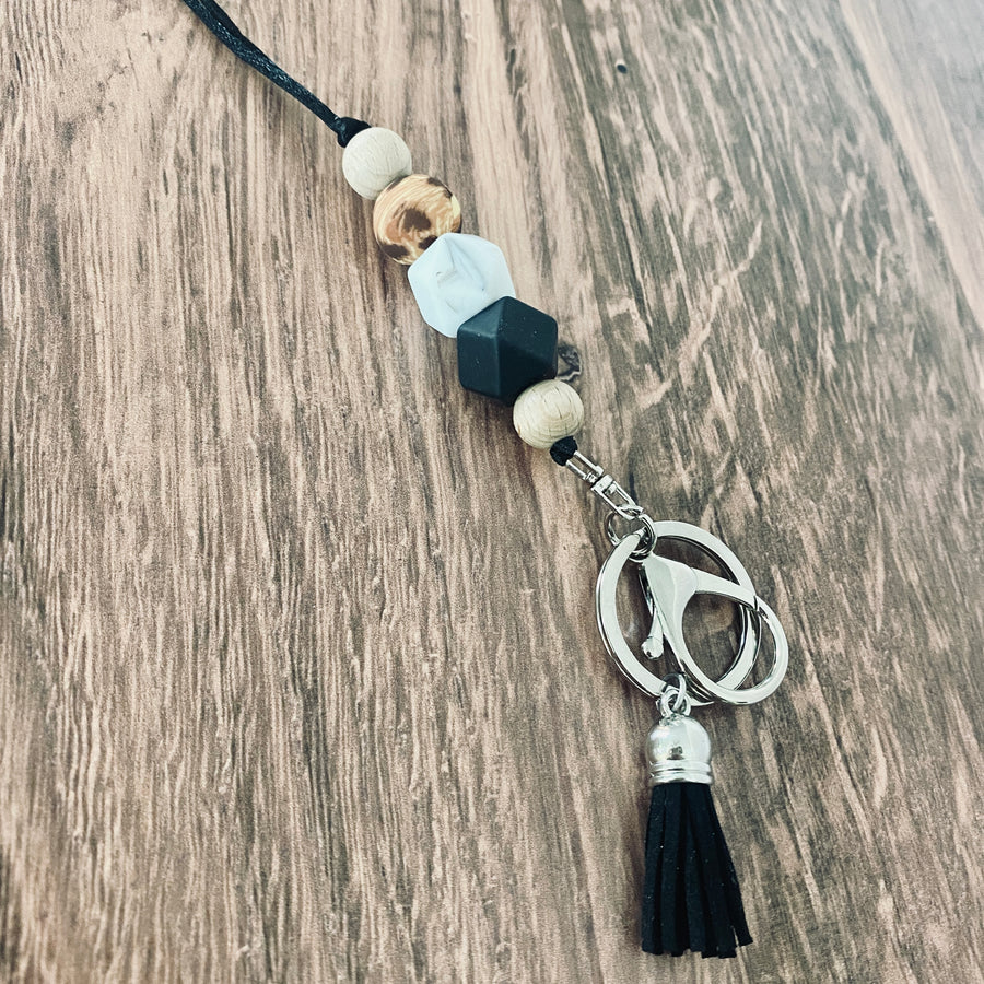 Cheetah print lanyard with a wood bead, cheetah print bead, marble hexagon bead, black hexagon bead, wood bead, and attached to a silver keyring and big lobster clasp with black suede tassel.