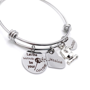 silver stainless steel bangle charm bracelet with a 3/4 inch charm engraved with a dandelion image and "let the wind be your guide", a 3/4 inch personalized heart name charm, graduation hat charm, and a .5 inch "2021" year charm