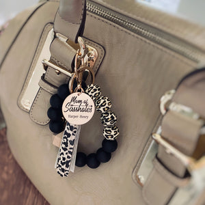 cheetah print and black silicone beaded wristlet with the engraved personalized tag with kids names "mom of sassholes" attached to a purse