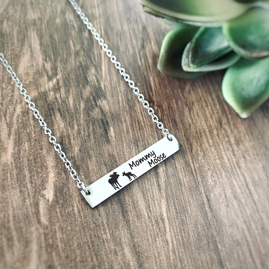 Silver horizontal bar necklace engraved with a mom moose and a baby moose with the verbiage "Mommy Moose" attached to a cable chain. Left side view