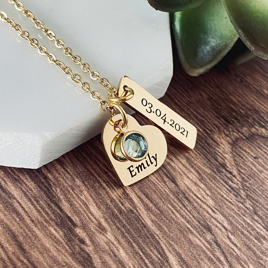 yellow gold stainless steel necklace with a 3/4 inch engraved heart with the name Emily and a march blue birthstone. Next to the heart hangs a 1.2" rectangle charm with the date of birth 3.4.21